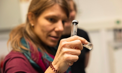 Woman holding a test tube in a laboratory setting, examining the contents closely